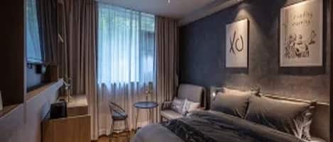 A modern hotel room with a large bed, a desk, a chair, and a small table.