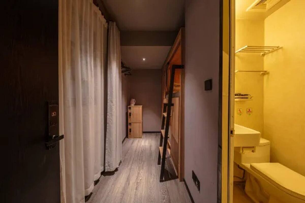 Un pasillo estrecho con piso de madera, una puerta a la izquierda y un baño a la derecha.
