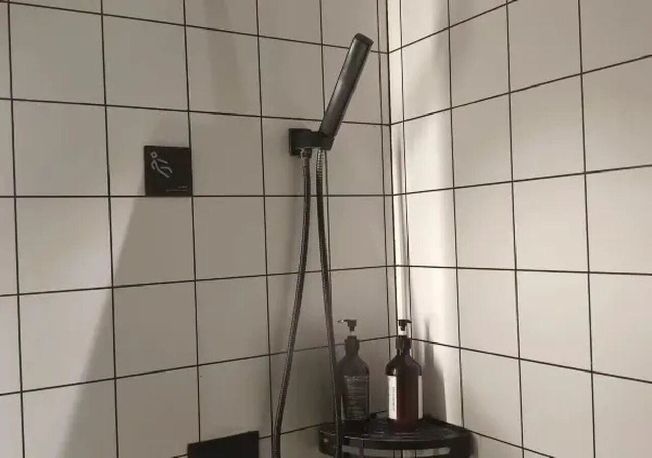 A tiled shower area with a handheld showerhead and a bottle of shampoo.