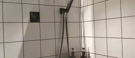 A tiled shower area with a handheld showerhead and a bottle of shampoo.