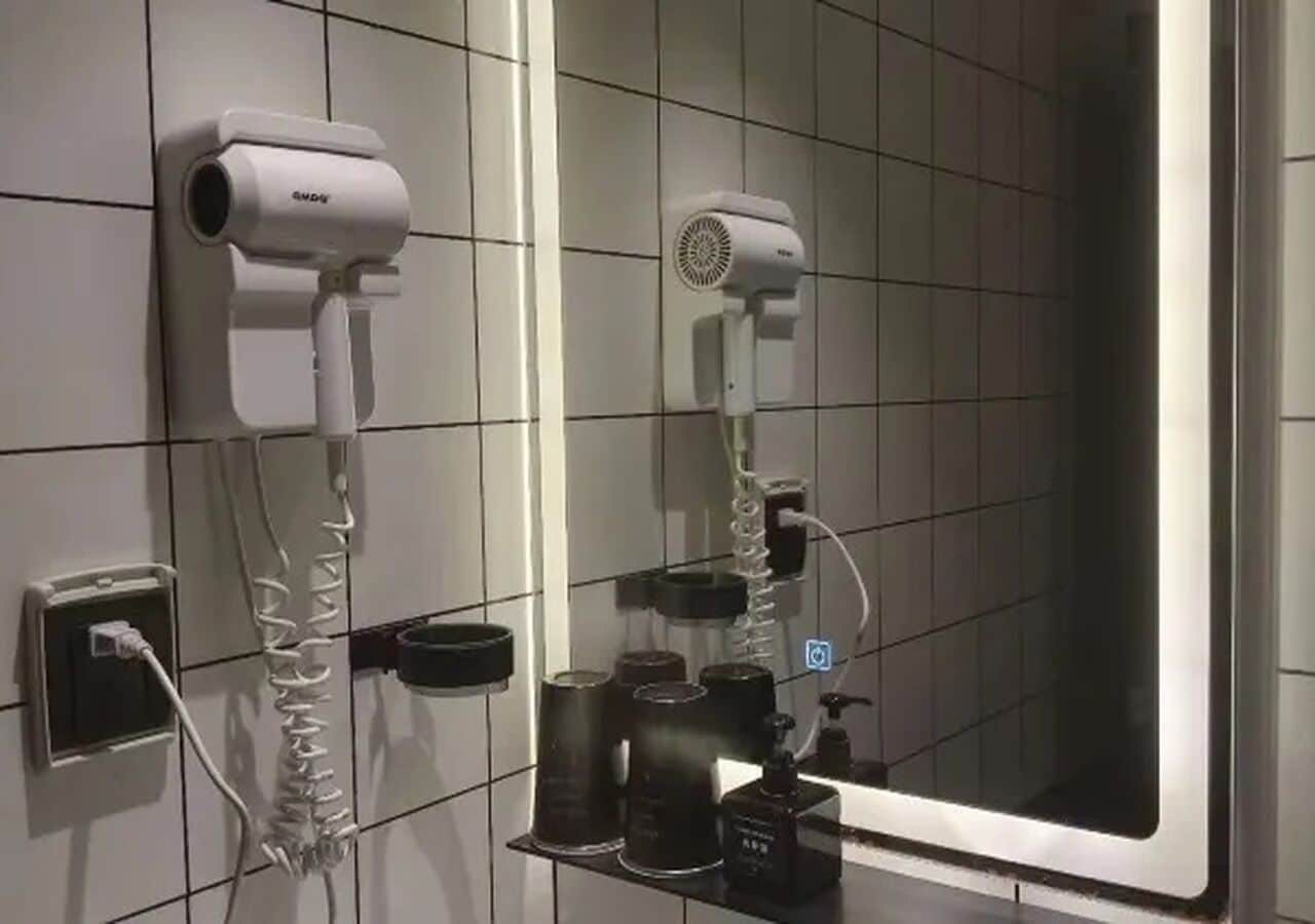Ein Badezimmer mit Spiegel, zwei Haartrocknern, einem Waschbecken und Pflegeprodukten.