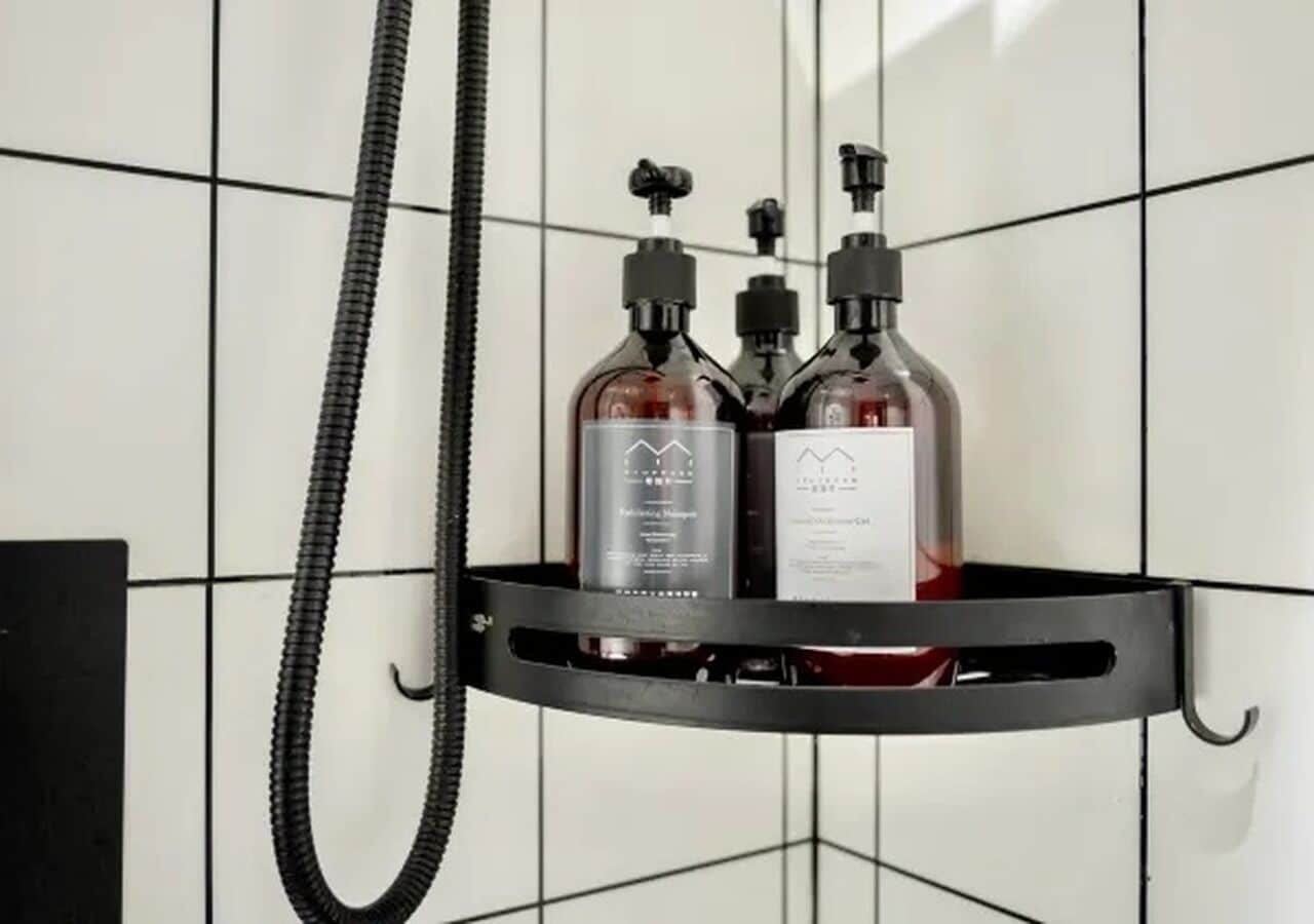 A bathroom with a black metal shelf holding two bottles of liquid soap and a black hose.