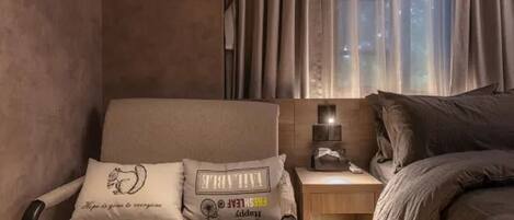 A cozy room with a chair, a bedside table with a lamp, and a bed.