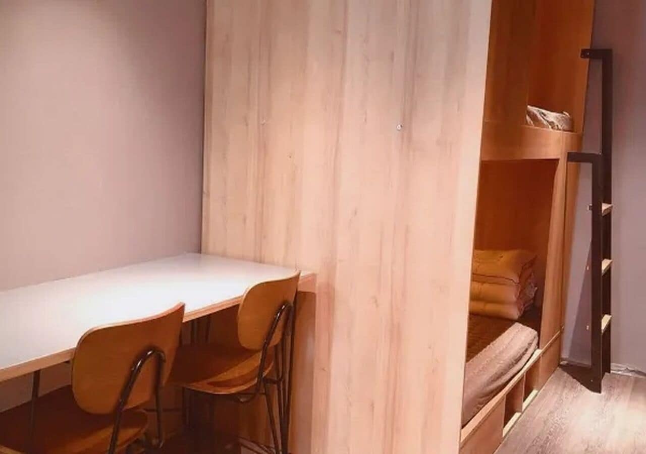 A room with a bunk bed, a desk with chairs, and a ladder.