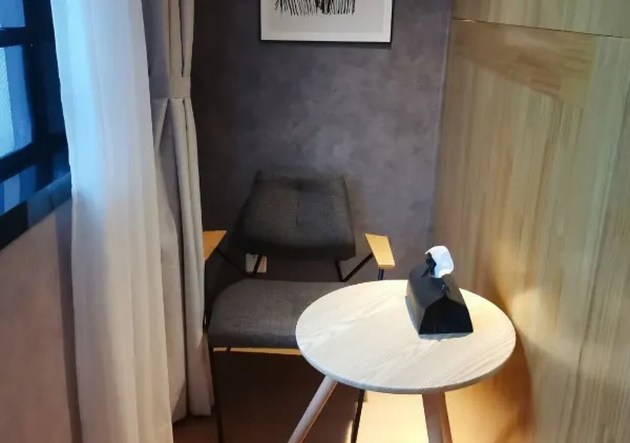 A room with a grey chair, a small white table, and a framed picture on the wall.