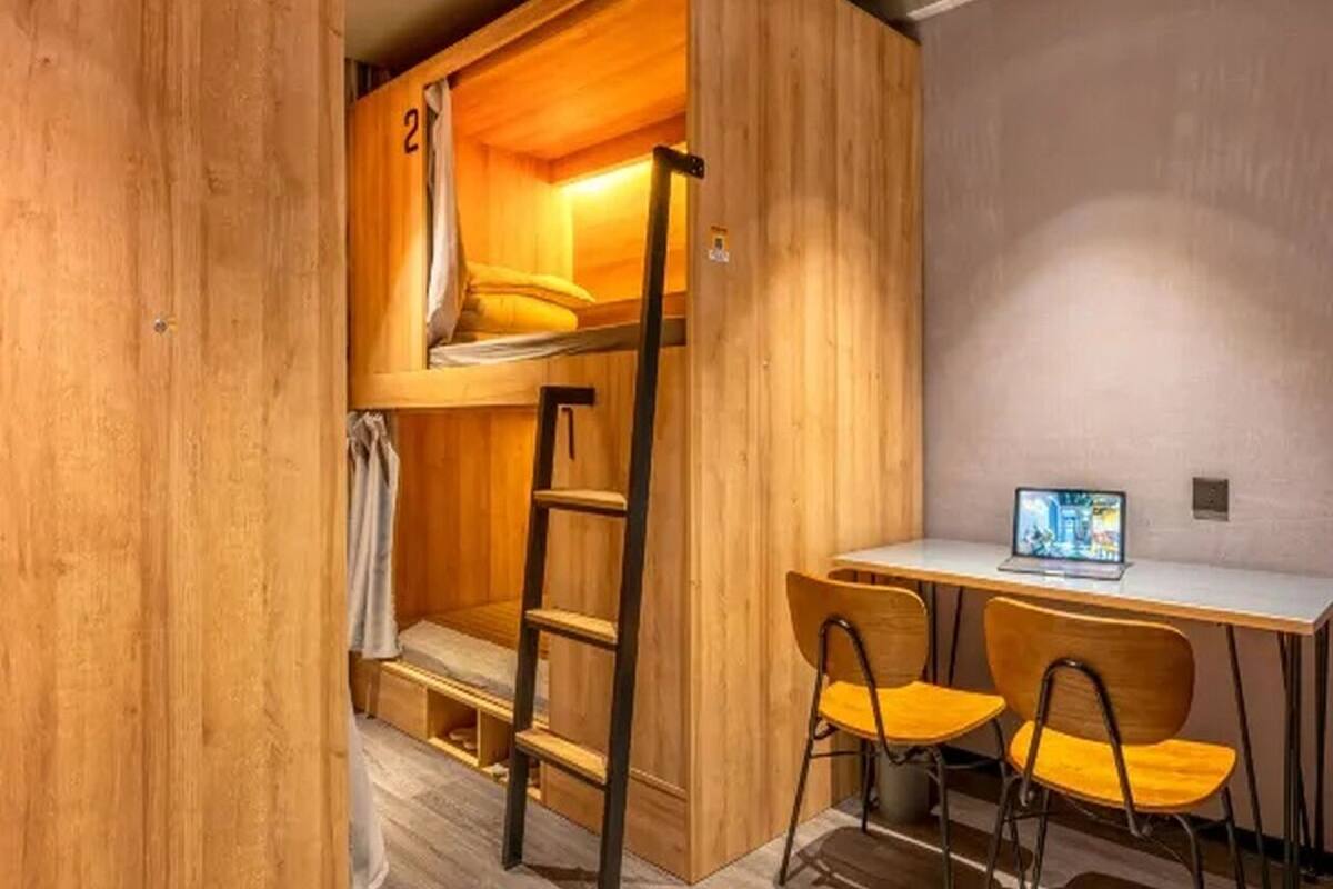 Un dormitorio con literas, una escalera, un escritorio, dos sillas y una computadora portátil.