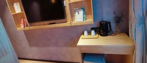 A compact room with a mounted television, a small wooden desk, and a trash bin.