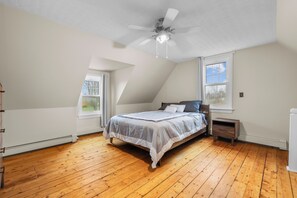 Ein Schlafzimmer mit einem Bett, Deckenventilator, Fenster und Holzboden.