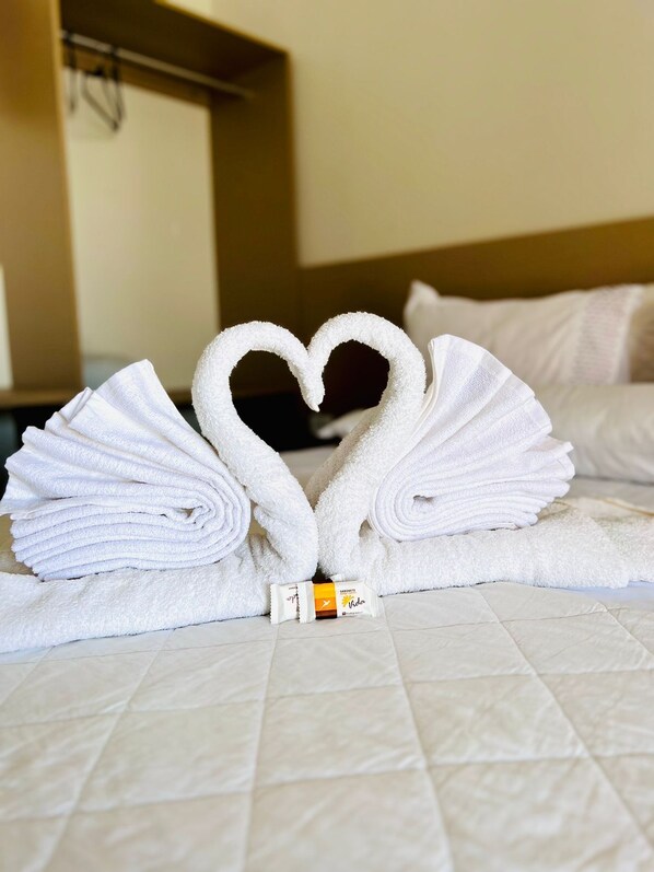 A hotel room with a bed, a heart-shaped towel arrangement, and a minibar.