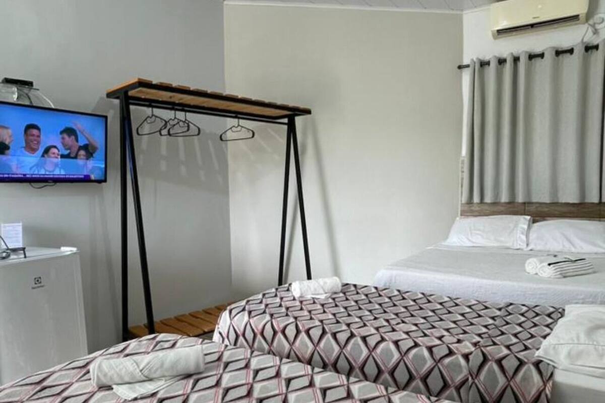 A hotel room with a bed, a TV, a hanging chair, and a window with curtains.