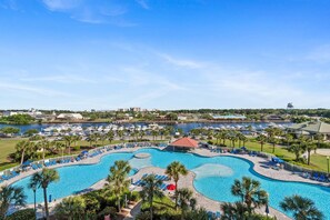 A large outdoor swimming pool with multiple lanes, surrounded by palm trees and lounge chairs, with a marina and buildings in the background. - Family Friendly Coastal Escape (North Myrtle Beach)