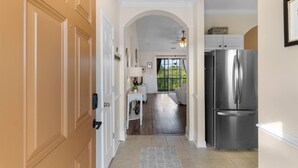 A hallway leading to a kitchen with a stainless steel refrigerator, a dining area with a table and chairs, and a view of greenery outside. - Family Friendly Coastal Escape (North Myrtle Beach)