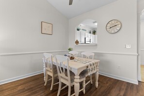 Een eetkamer met een witte tafel, vier stoelen, een klok en een lijst met een afbeelding aan de muur.