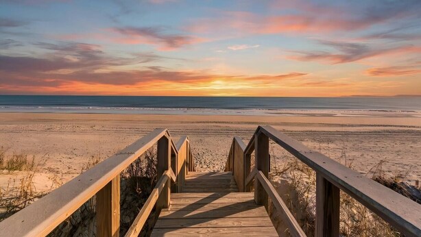 A wooden boardwalk leading to a beach with a sunset in the background. - Family Friendly Coastal Escape (North Myrtle Beach)