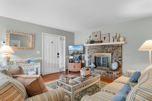 A living room with a fireplace, striped sofas, a coffee table, and a television. - North Myrtle Beach Cottage 2 Blocks From Beach (North Myrtle Beach)