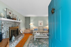 A cozy living room with a fireplace, a blue door, a striped sofa, and a patterned rug. - North Myrtle Beach Cottage 2 Blocks From Beach (North Myrtle Beach)