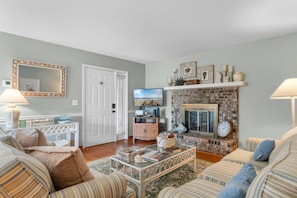 A living room with a fireplace, striped sofas, a coffee table, and a television. - North Myrtle Beach Cottage 2 Blocks From Beach (North Myrtle Beach)