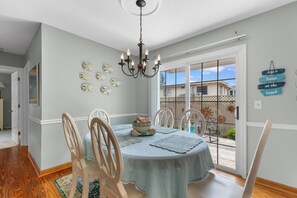 A dining area with a round table, chairs, a chandelier, and a view of the backyard through glass doors. - North Myrtle Beach Cottage 2 Blocks From Beach (North Myrtle Beach)