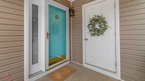 Una entrada de casa con una puerta verde azulada, una puerta blanca con un adorno festivo, y un pequeño porche.