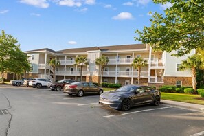 Ein mehrstöckiges Hotel mit Balkonen, einem Parkplatz mit mehreren Autos und Palmen.