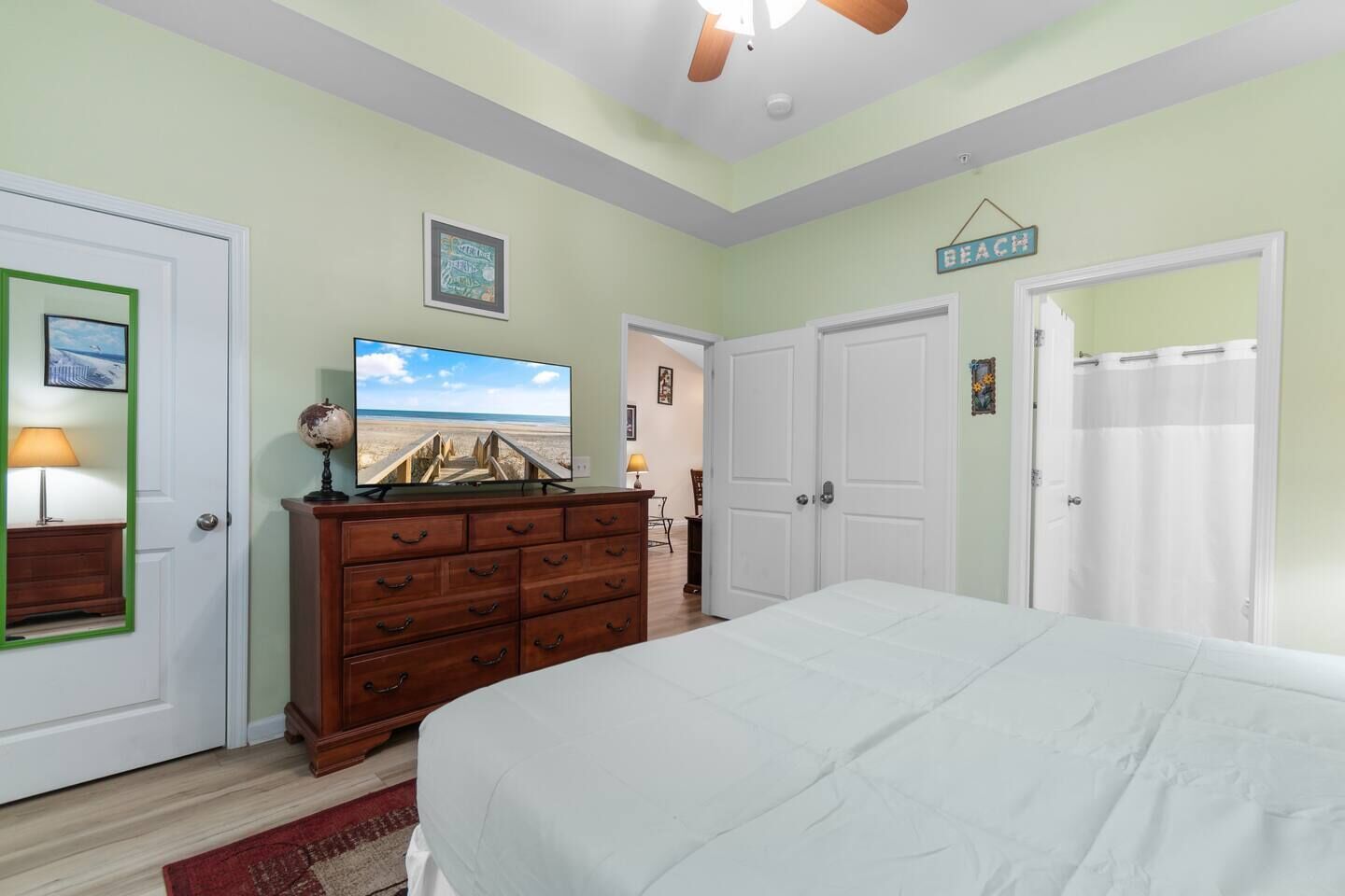 Une chambre à coucher comprenant un lit, une commode, un téléviseur et une porte ornée d’une enseigne sur le thème de la plage.
