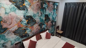 A hotel room with a bed, a nightstand, a chair, a ceiling fan, and a large abstract painting on the wall.