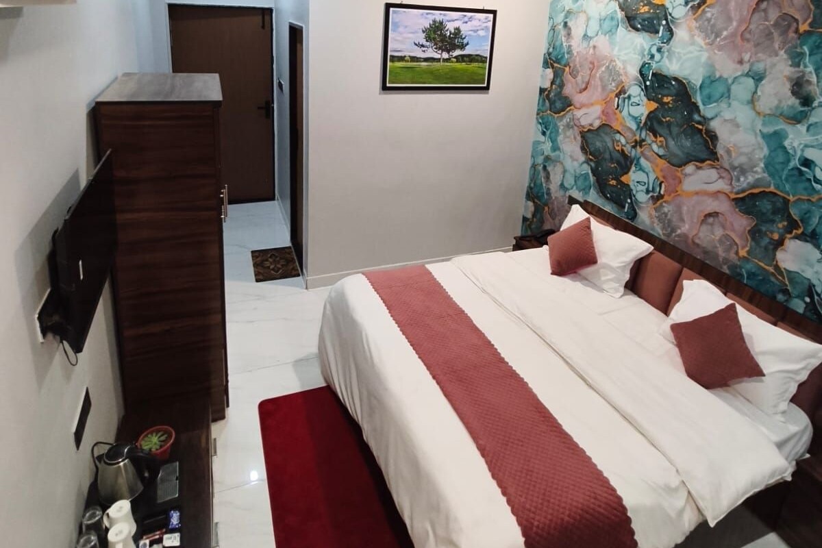 A bedroom with a bed, a ceiling fan, a TV, a painting, and a small table with items on it.