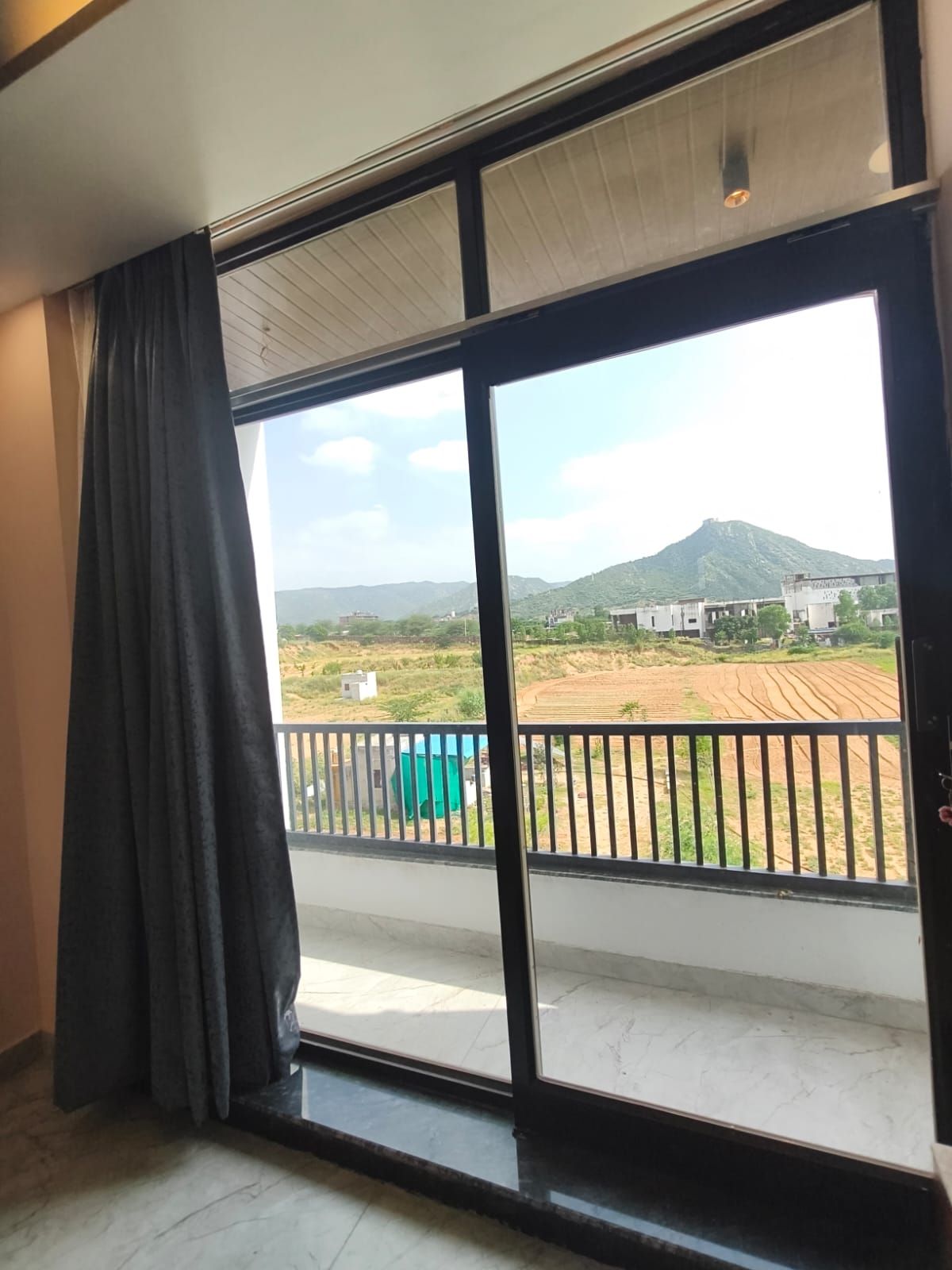 A room with a large sliding glass door leading to a balcony with a view of a field and a mountain.