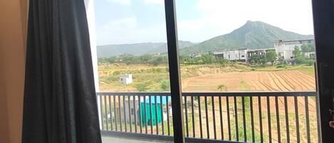 A room with a large sliding glass door leading to a balcony with a view of a field and a mountain.