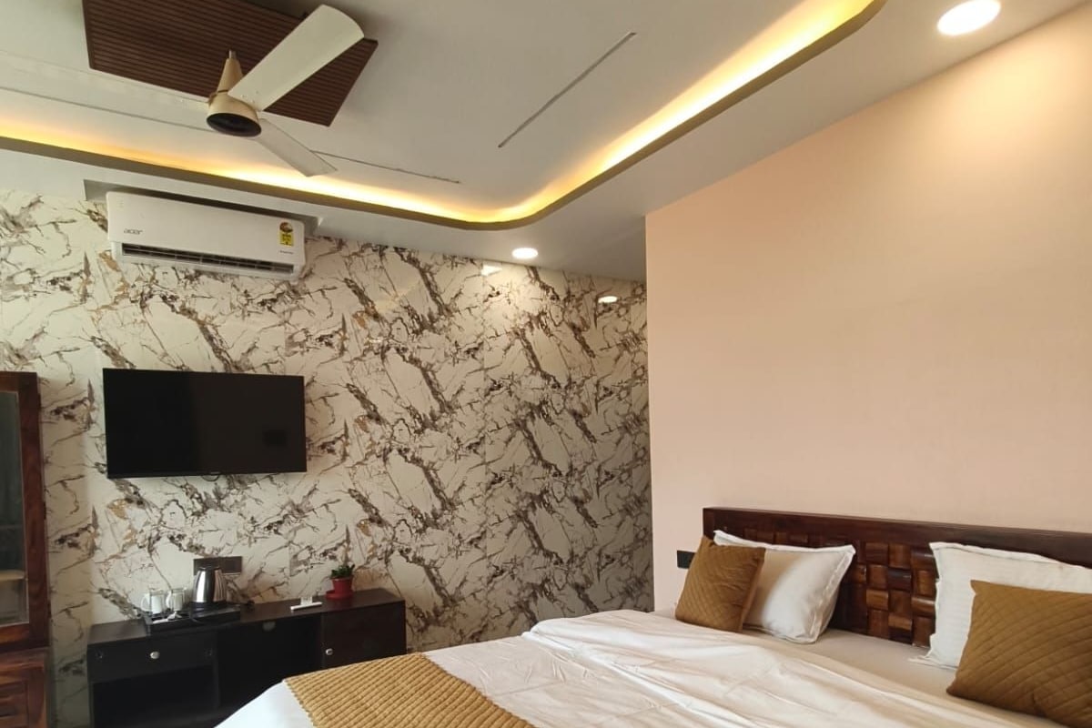 A hotel room with a bed, a flat-screen TV mounted on the wall, a ceiling fan, and an air conditioning unit.