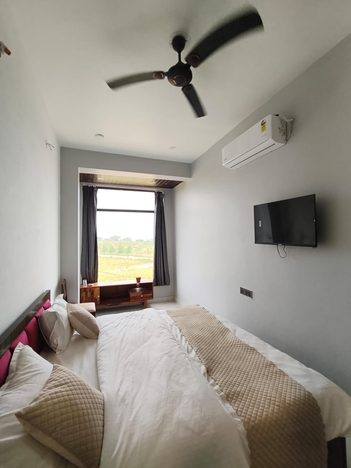 A bedroom with a bed, a ceiling fan, a TV, and a window with curtains.