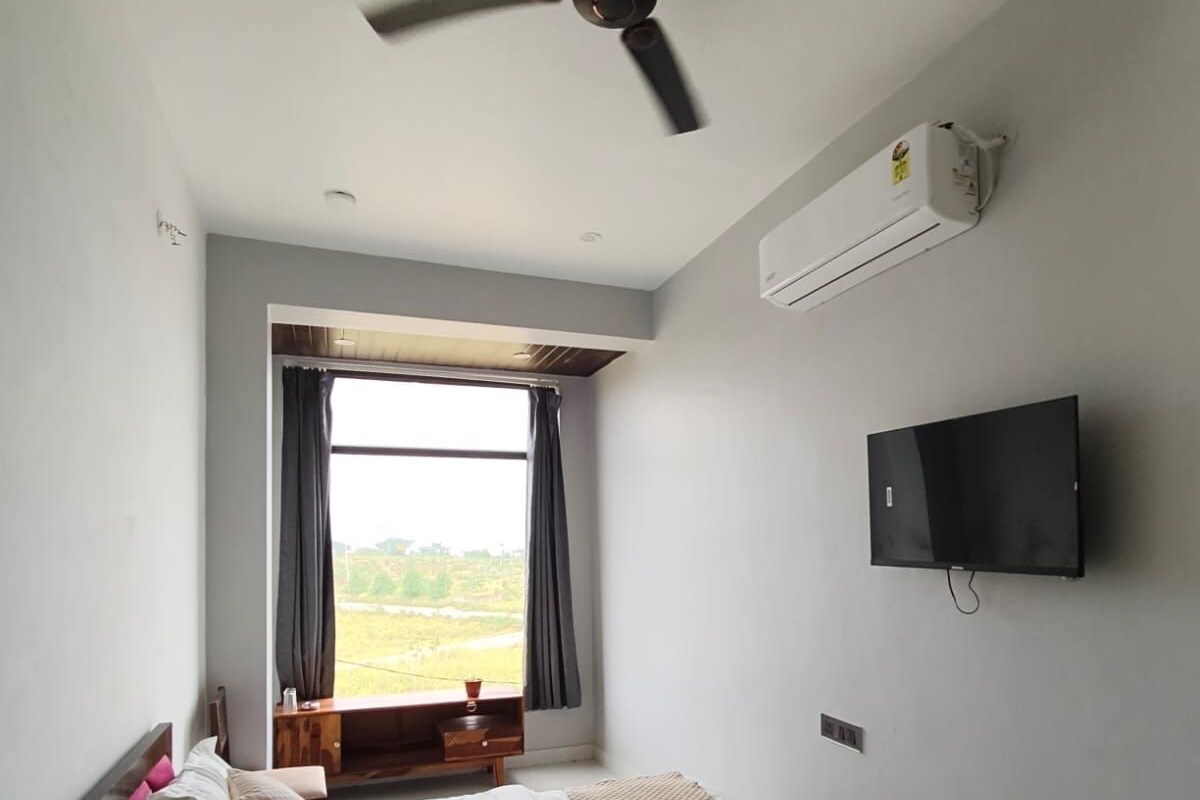 A bedroom with a bed, a ceiling fan, a TV, and a window with curtains.