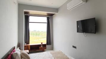 A bedroom with a bed, a ceiling fan, a TV, and a window with curtains.