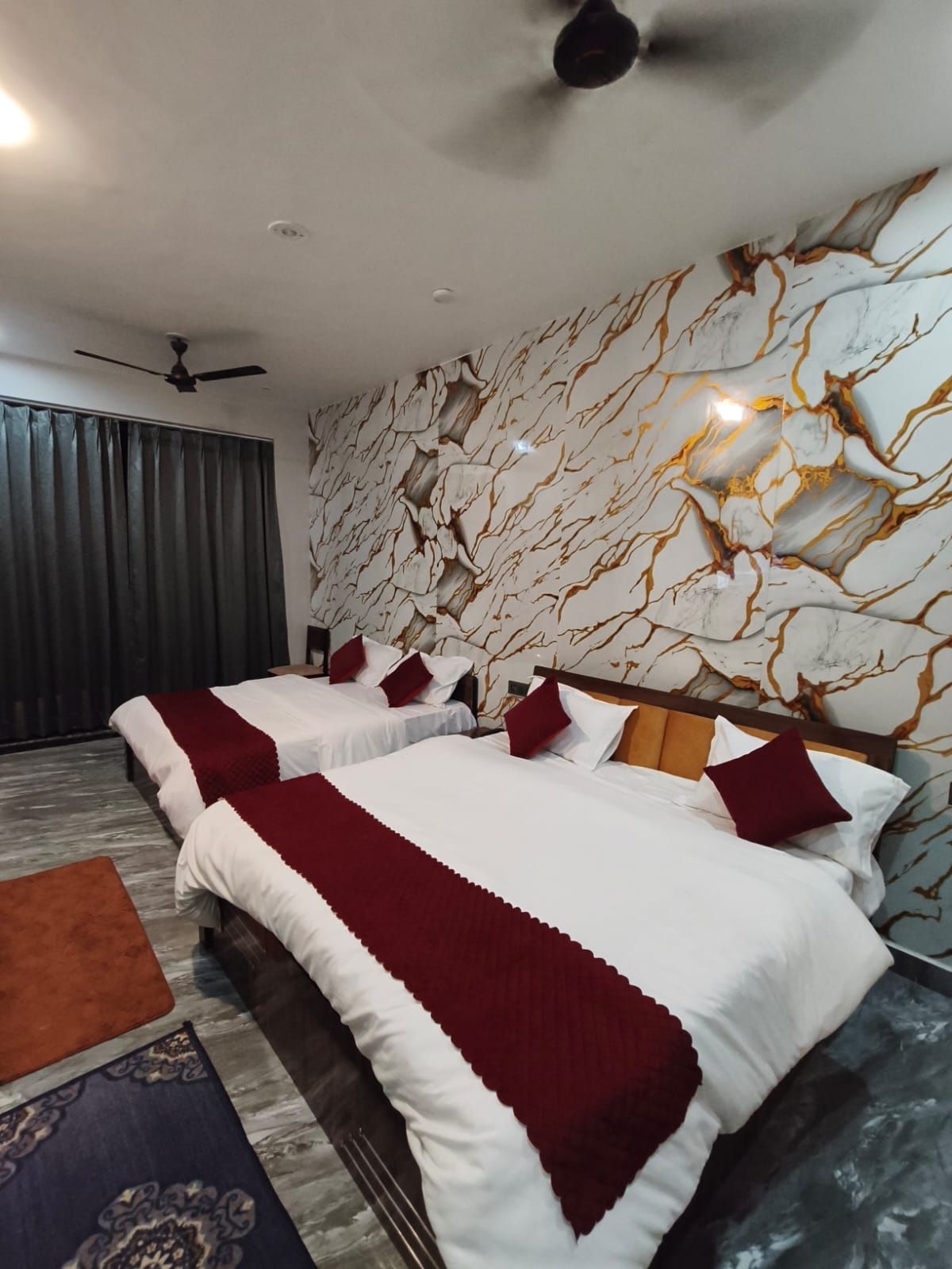 A hotel room with a bed, a ceiling fan, a wall with a marble-like pattern, and a window with curtains.
