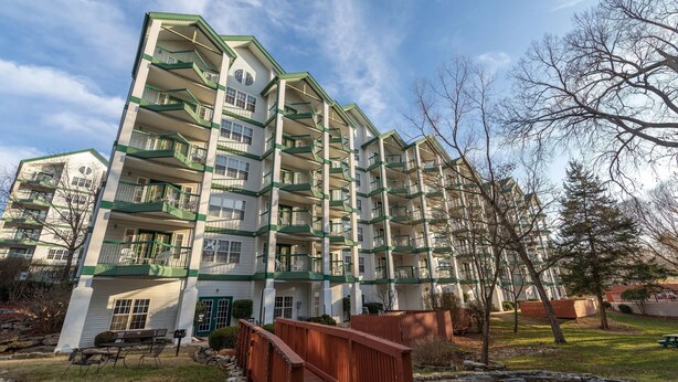 Ein mehrstöckiges Wohngebäude mit Balkonen, einer Holzbrücke und einer Rasenfläche.