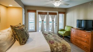 Ein Hotelzimmer mit einem Bett, einem Fernseher, einem grünen Sessel, einer Holzkommode und einem Deckenventilator.