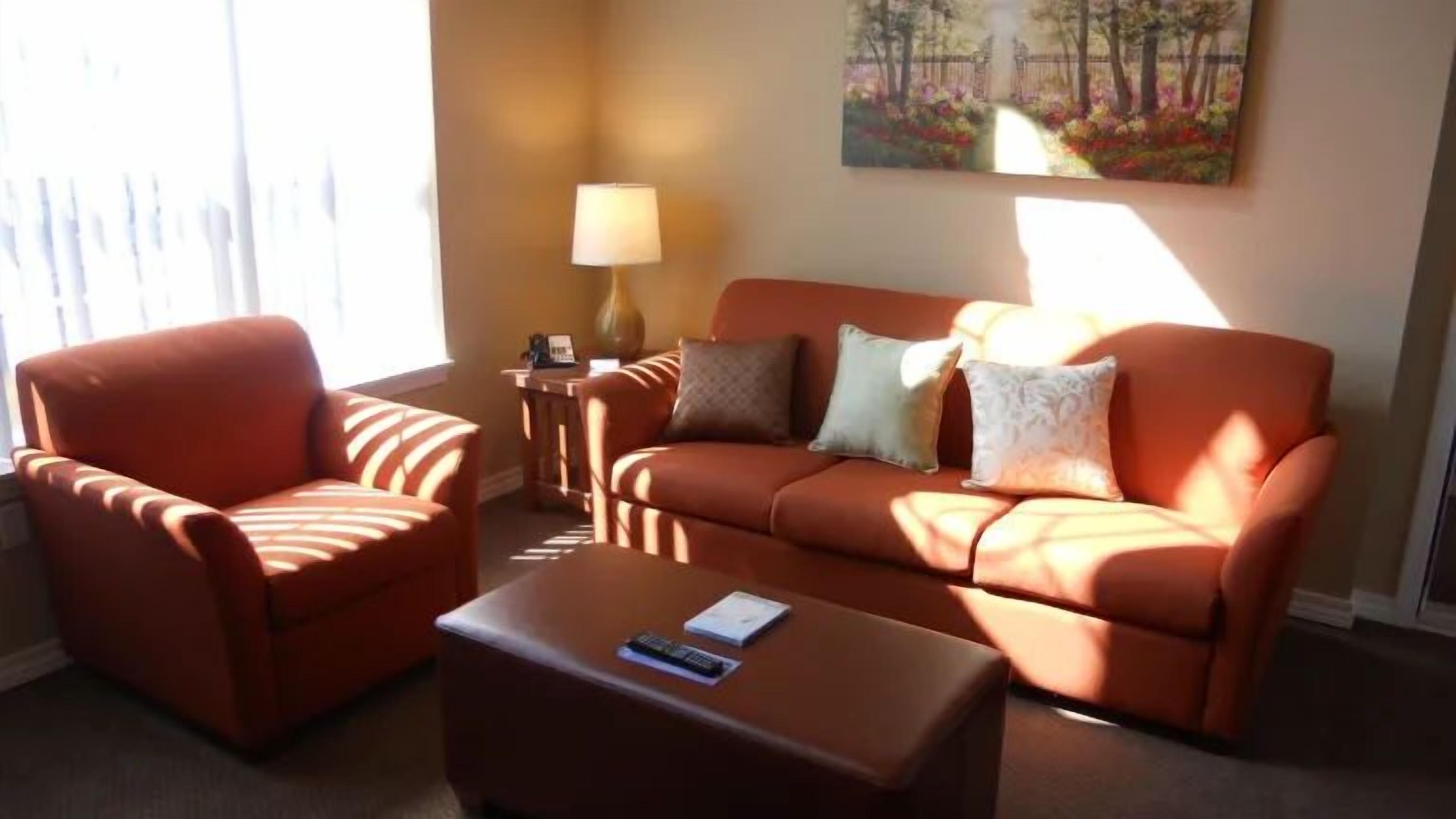 A living room with a sofa, armchair, and ottoman, a lamp, and a painting on the wall.