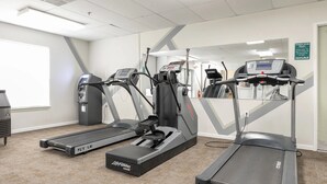 Une salle de remise en forme équipée de tapis de course, d’un vélo d’appartement et d’un mur recouvert de miroirs.