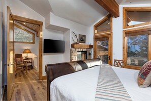Quarto com uma cama grande, televisão, lareira e vigas de madeira.