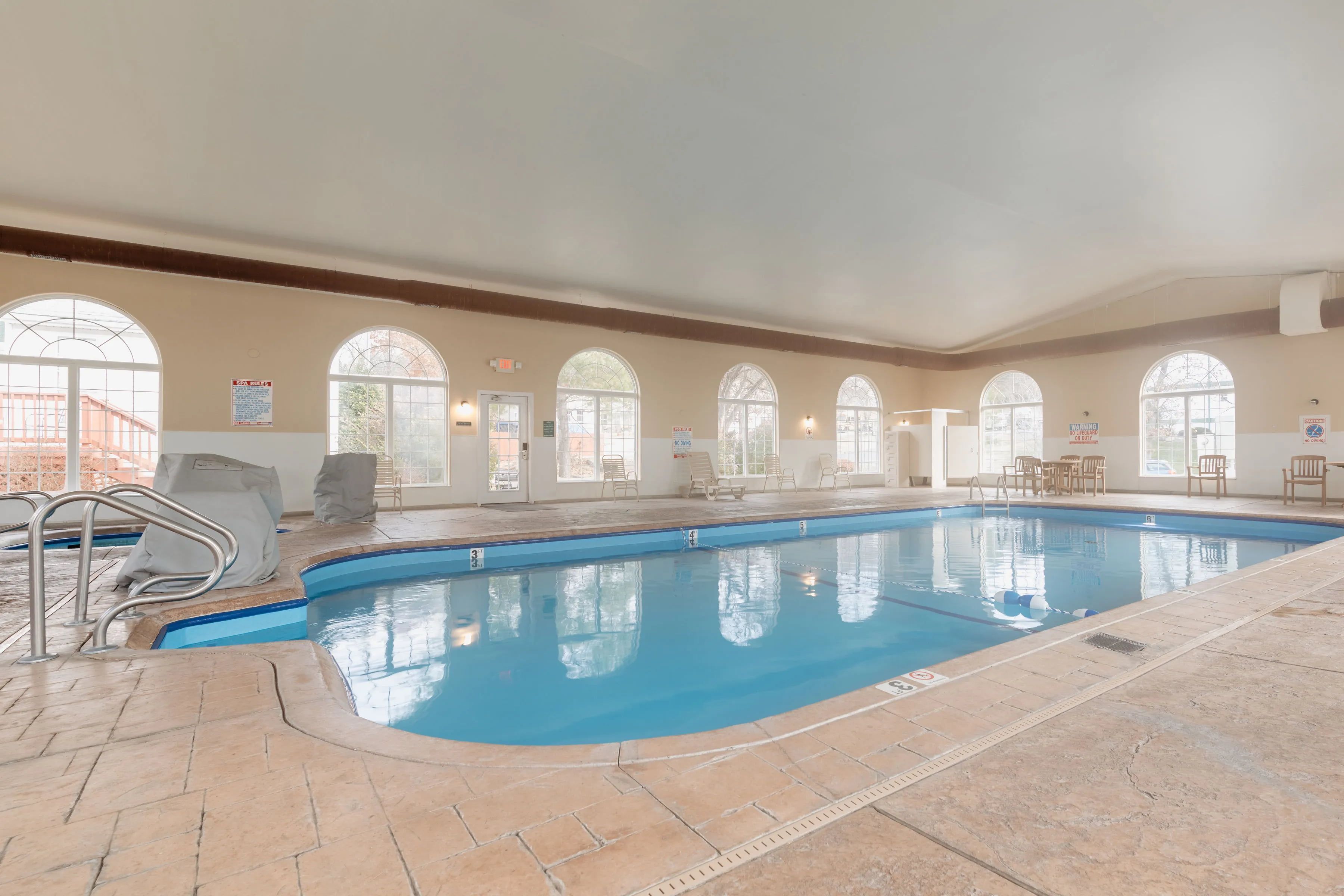 An indoor swimming pool with clear water, tiled floor, and arched windows.