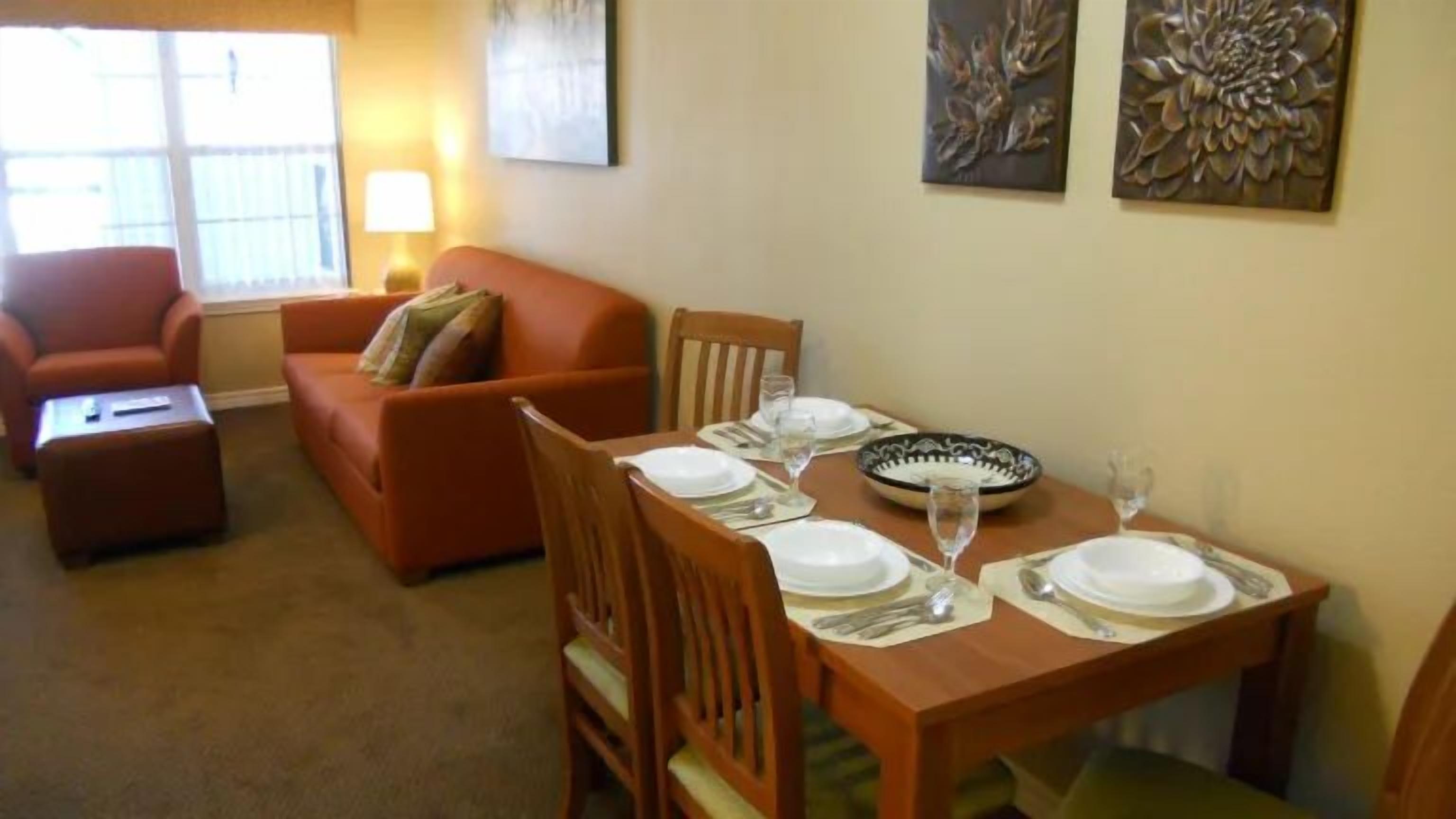 Un comedor con una mesa dispuesta para cuatro personas, un sofá y una lámpara.