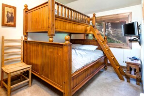 A bunk bed with a wooden ladder, a wooden chair, a television on a stand, and a window with a view of a stone wall and greenery. - KBM Resorts | In the Heart of Old Town, Walk to Main St., Easy access shuttle to PCMR or DV Resorts, Private Hot Tub! POA-504b (Park City)