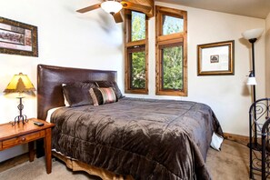 A bedroom with a large bed, a ceiling fan, a nightstand with a lamp, and a window with a view of trees. - KBM Resorts | In the Heart of Old Town, Walk to Main St., Easy access shuttle to PCMR or DV Resorts, Private Hot Tub! POA-504b (Park City)
