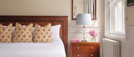 A bedroom with a large bed, bedside table, lamp, and a window with curtains.