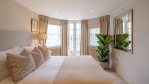 Ett hotellrum med en stor säng, en krukväxt, en spegel och ett fönster med gardiner.