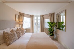 Ein Hotelzimmer mit einem großen Bett, einer Zimmerpflanze, einem Spiegel und einem Fenster mit Vorhängen.