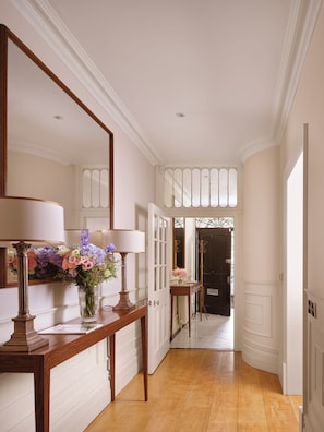 A hallway with a wooden console table, a mirror, and a vase of flowers. - Mayfair's Finest | Magnificent Georgian Townhouse (London)