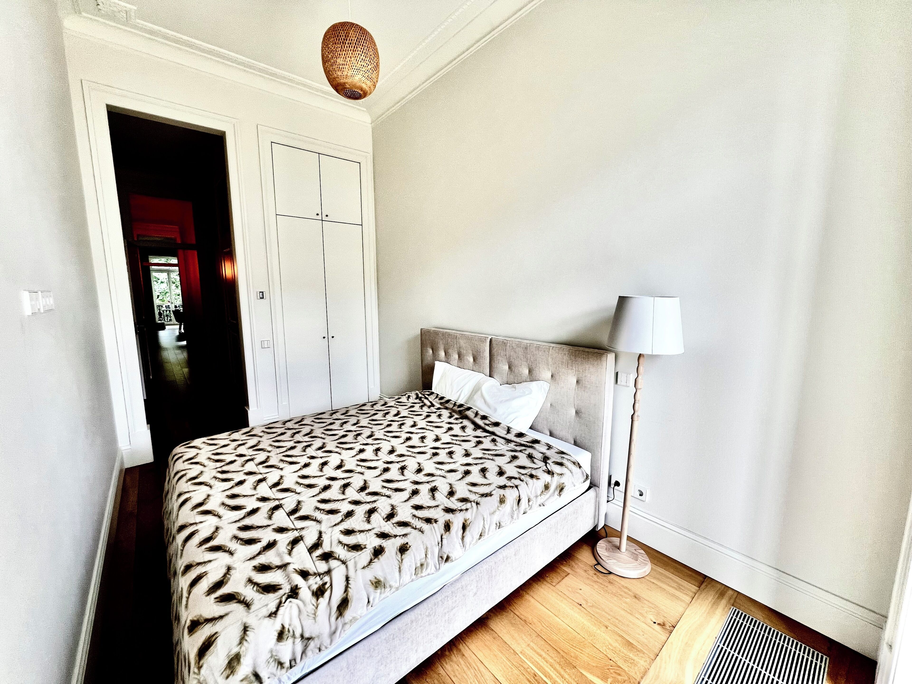 Een slaapkamer met een bed, bedlampje, kledingkast en een plafondlamp.