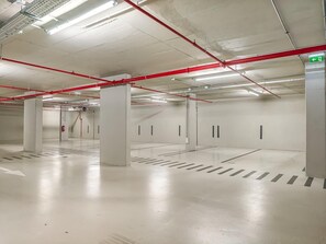 A spacious parking garage with clear directional arrows on the floor, red safety railings, and a fire extinguisher mounted on the wall. - Luxury 3-Bedroom Apartment in Prime Central Lisbon | Terrace, Pool, Gym, and Private Parking (Lisboa)