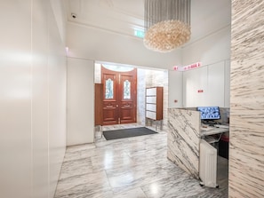 Eine Hotellobby mit Marmorboden, zweiflügeligen Holztüren, einem Empfangstresen und einer modernen Pendelleuchte.